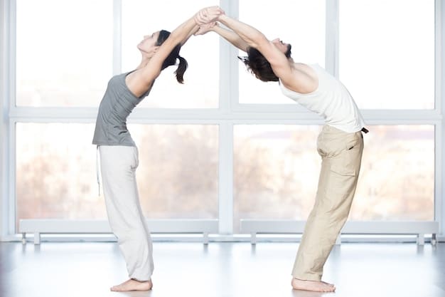 A couple performing a standing forward fold in partner yoga, with one partner supporting the other's back, creating a sense of support and connection.