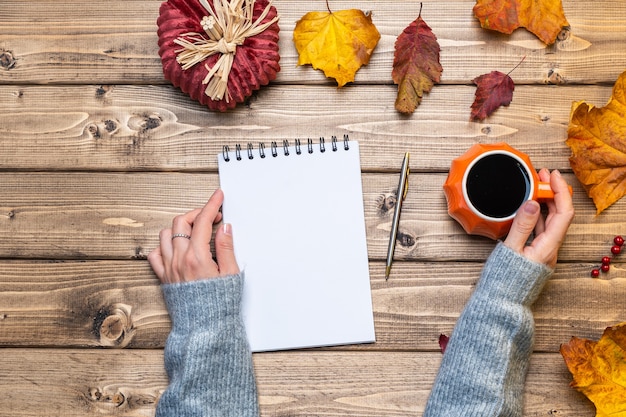 A close-up shot of hands writing in a gratitude journal on a wooden desk, with a cup of coffee, a pen, and a small potted plant nearby. The journal is open to a page with bullet points and handwritten text.
