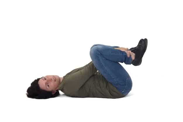 A person lying on their back with knees bent, one hand on their chest and the other on their abdomen, demonstrating the hand placement for diaphragmatic breathing. The image is taken from a slightly elevated angle.
