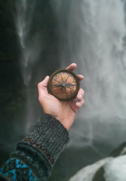 A hand holding a compass, pointing towards a distant mountain peak. The compass symbolizes guidance and direction, while the mountain represents a challenging goal or aspiration.