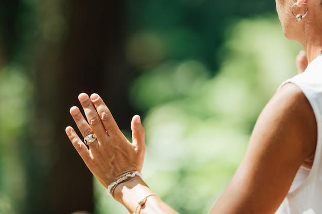 A close-up shot of hands in a prayer position (Anjali mudra) against a backdrop of lush greenery and a blurred coastline, symbolizing mindfulness and connection with nature during a yoga retreat.