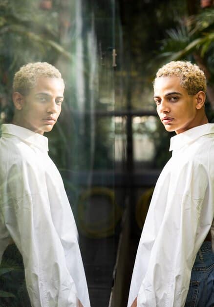 A person looking in a mirror, seeing a confident and strong reflection of themselves. The background is a blurred image of their current, less confident self.