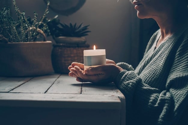 A person meditating in a peaceful environment with soft, natural light. They are surrounded by plants and candles, creating a serene atmosphere.