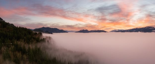 A panoramic view of a serene mountain landscape at dawn, with mist rising from a valley below, evoking a sense of peace and awe.