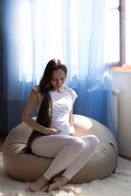 A close-up shot of a pregnant woman in her first trimester sitting comfortably in a cross-legged position, performing a gentle breathing exercise with her hands resting on her knees. She has a serene expression, and the focus is on her posture and hand placement.