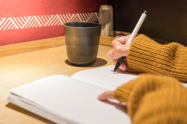 A close-up of a person journaling, with a pen in hand and a notebook open on a desk. The background is blurred, focusing on the act of writing and reflection.