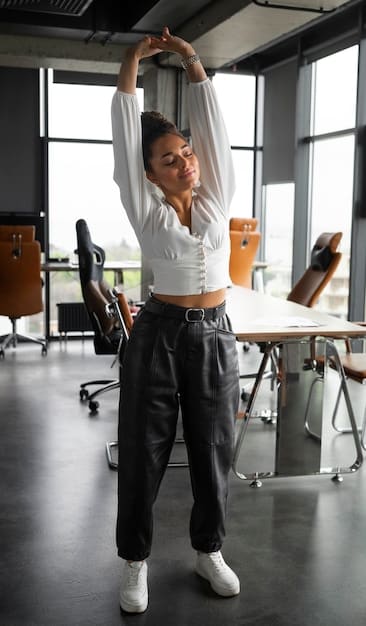 A person stands in a sunny office, gracefully performing a standing side stretch. They are reaching one arm overhead while gently bending to the side, showcasing flexibility and relaxation amidst the workplace.