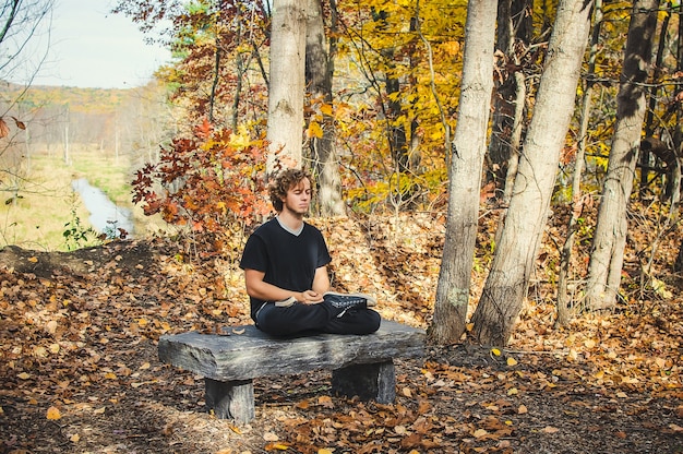 A person meditating peacefully in a park, away from electronic devices, with sunlight filtering through the trees.