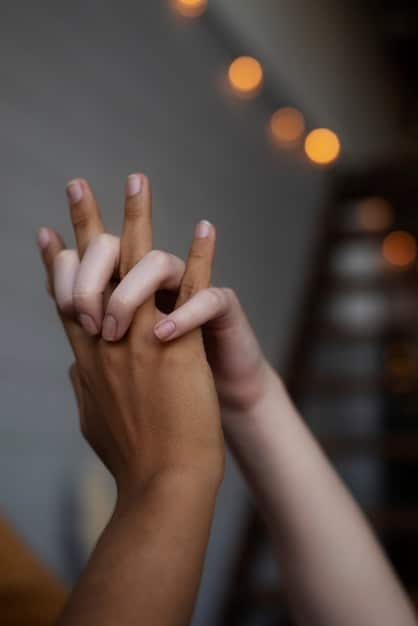 A close-up shot of hands gently pressing together in a meditative pose, with a soft, blurred background showing a serene natural setting. The hands are slightly illuminated, creating a sense of peace and focus.