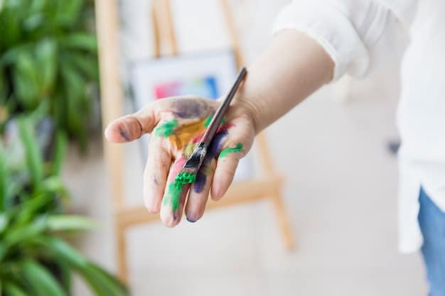 A close-up shot of a person's hands gently holding a paintbrush over a canvas. The background is blurred, emphasizing the focused attention and meditative state of the artist.