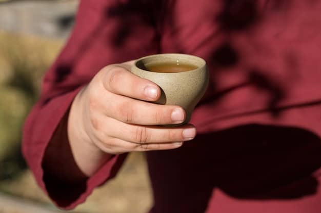 Close-up shot of a person's hands gently holding a teacup during a mindful tea ceremony. The focus is on the hands and the cup, with a blurred background suggesting a calm and peaceful setting.