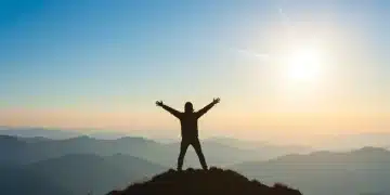 Person confidently standing on a mountain peak, symbolizing boosted self-efficacy and achievement.